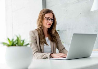 woman with glasses sitting at desk using laptop